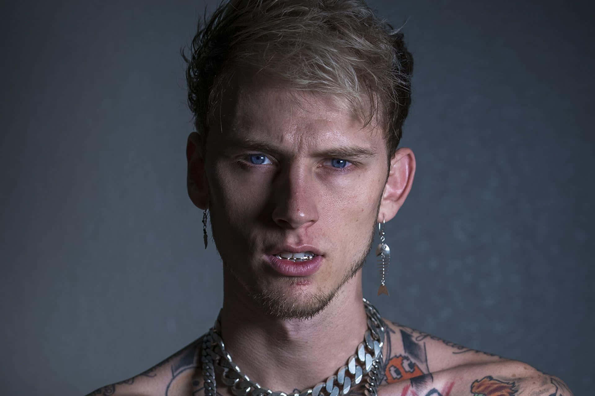 mgk 桌布 壁紙 — 一位藍眼睛、有刺青的年輕男子在深灰色背景下強烈凝視。