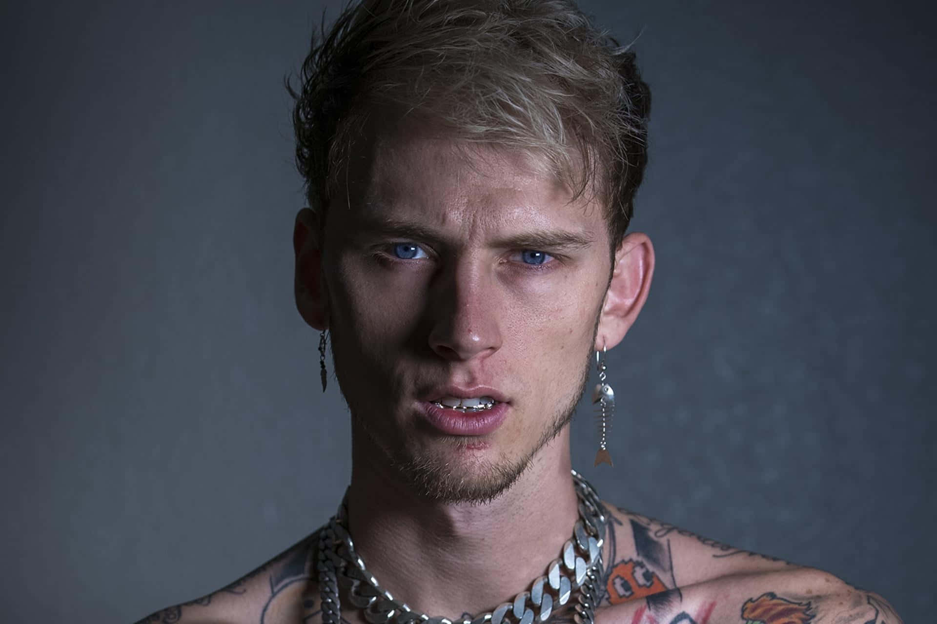mgk 桌布 壁紙 — 一位藍眼睛、有刺青的年輕男子在深灰色背景下強烈凝視。