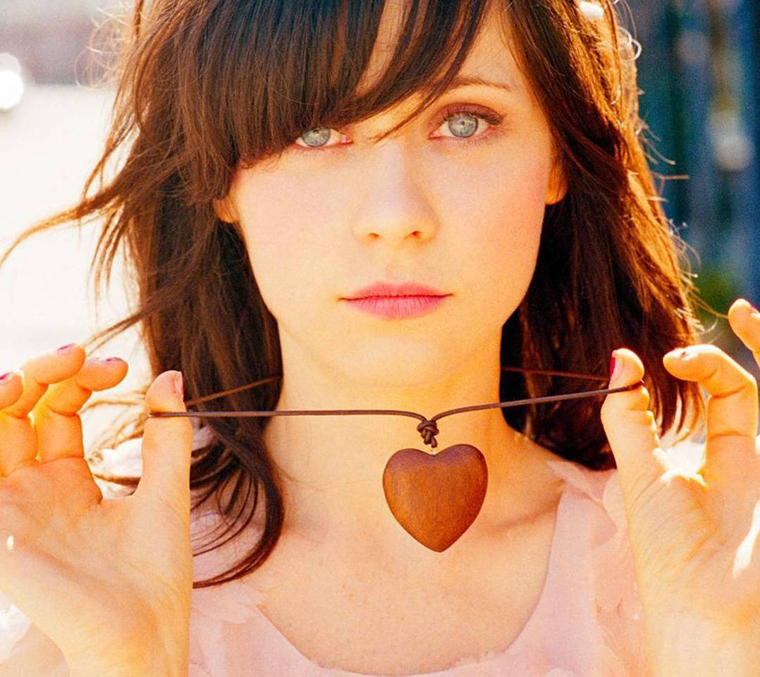 Cute Heart 桌布 壁紙 — 一位藍眼睛、棕色頭髮的年輕女性在柔和的金色陽光下拿著木製心形項鍊。