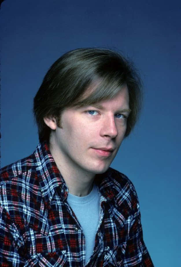 Michael Mckean 桌布 壁紙 — 一位藍眼睛、棕色頭髮的年輕男子穿著紅藍白格紋襯衫，背景是純藍色攝影棚。