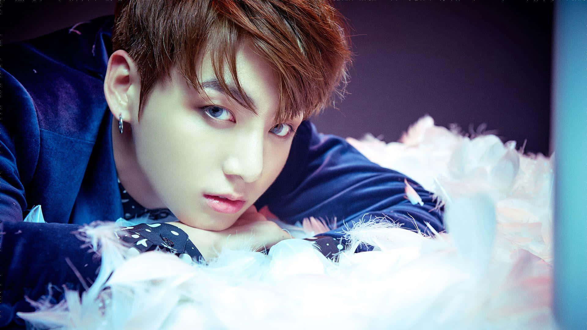 Jungkook 桌布 壁紙 — 一位藍眼睛、棕色頭髮的年輕男子躺在白色羽毛上，穿著深藍色天鵝絨服裝。