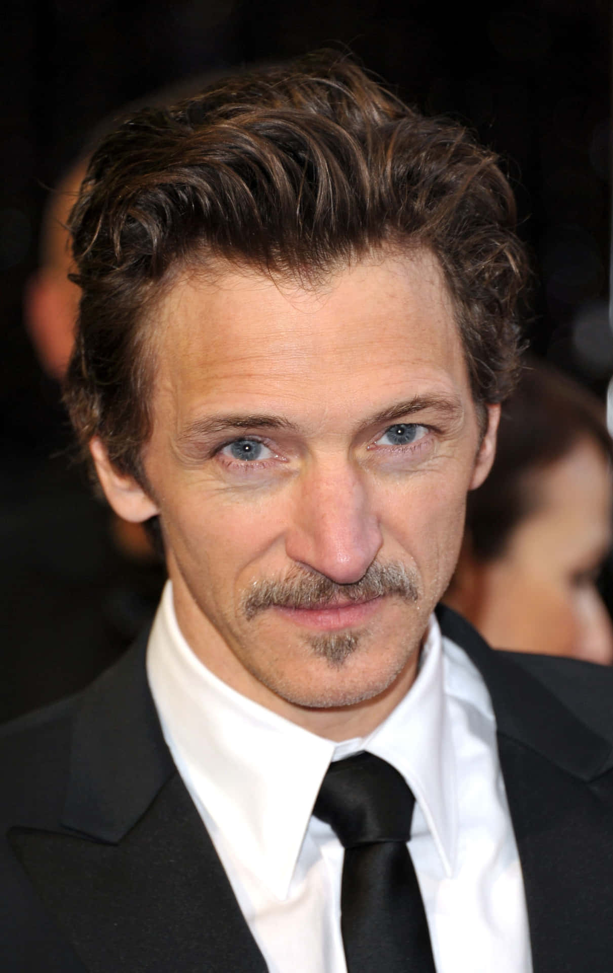John Hawkes 桌布 壁紙 — 一位藍眼睛、留鬍子的男士近距離肖像，身穿黑色西裝和白色襯衫。