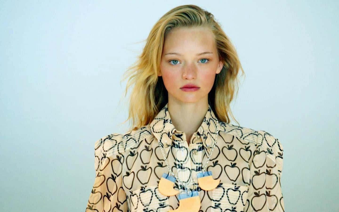Gemma Ward 桌布 壁紙 — 一位藍眼睛的金髮女性，穿著米色蘋果圖案襯衫，背景是柔和的藍色。