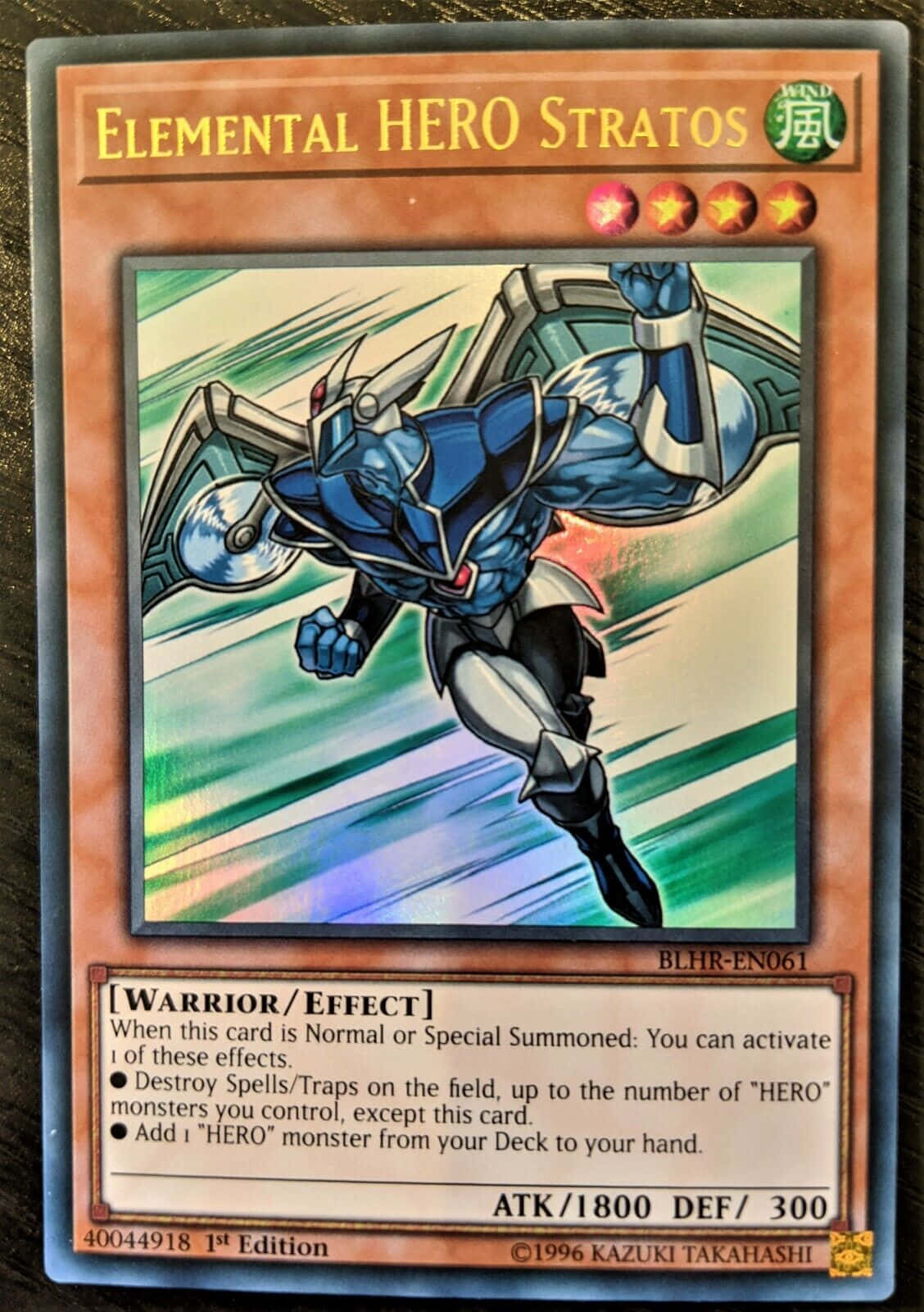 Yugioh Elemental Hero 桌布 壁紙 — 一位藍色裝甲英雄，帶著翅膀和盾牌，在綠色和藍色條紋背景上向前衝刺。