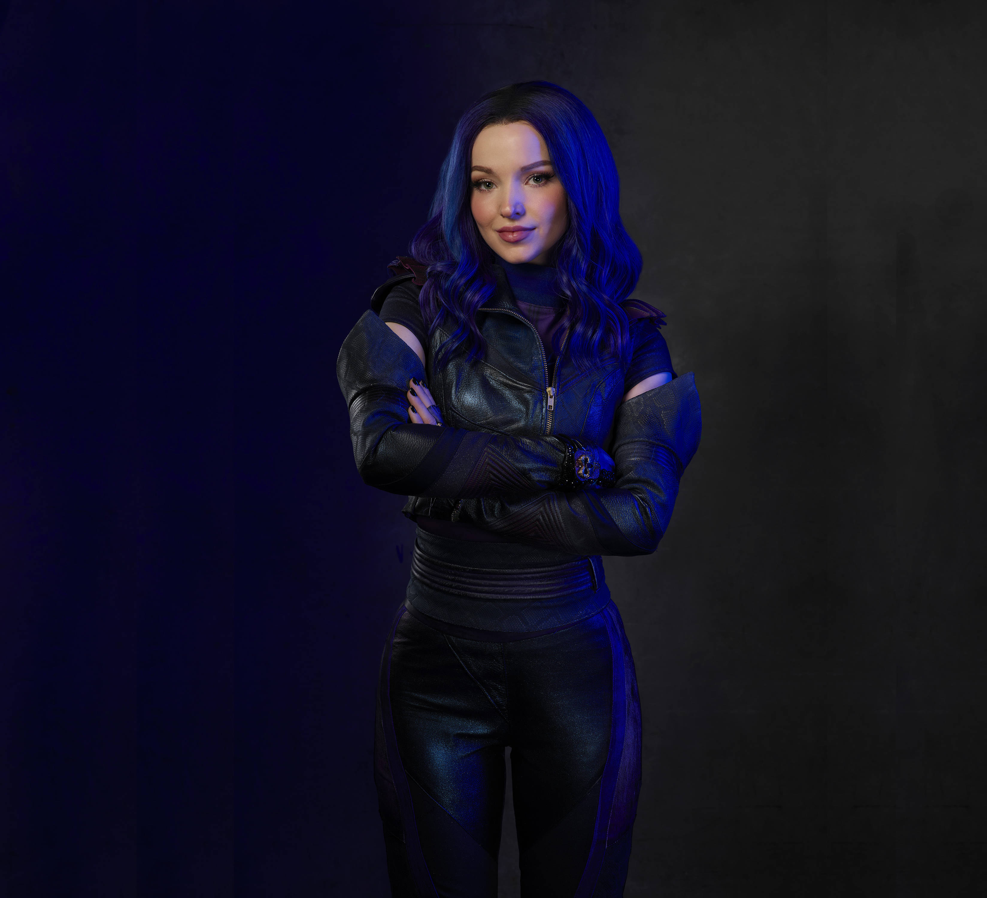 Descendants 桌布 壁紙 — 一位藍色頭髮、穿著皮革服裝的女性，在深藍色背景前自信地交叉雙臂站立。