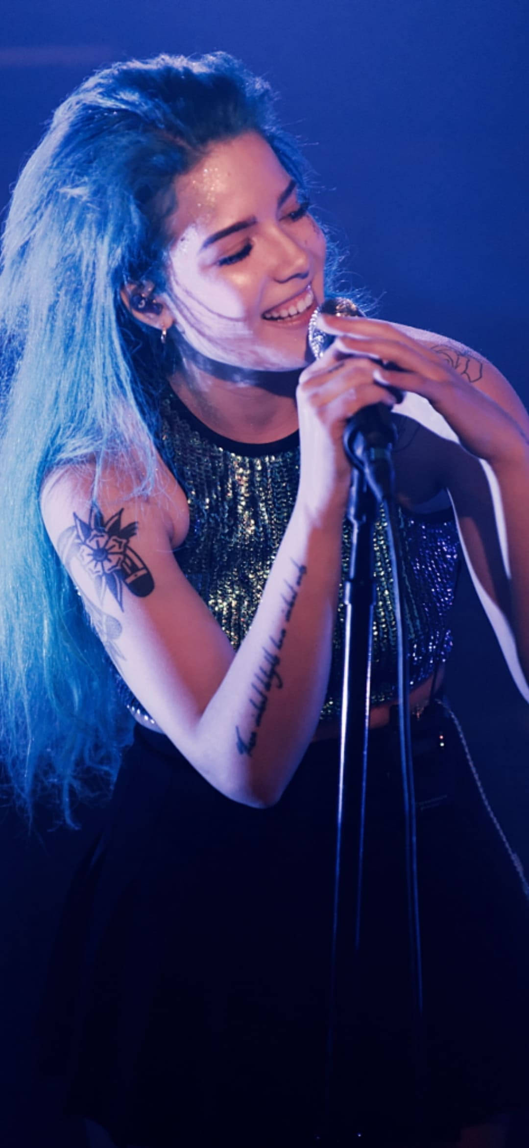 Halsey 桌布 壁紙 — 一位藍髮、有刺青的女歌手在藍色舞台燈光下熱情地對著麥克風演唱。