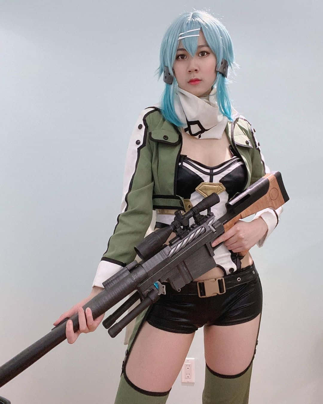 Sword Art Online Cosplay 桌布 壁紙 — 一位藍髮、身穿戰術裝備的角色扮演者，手持狙擊步槍靠著一面素灰色牆壁。
