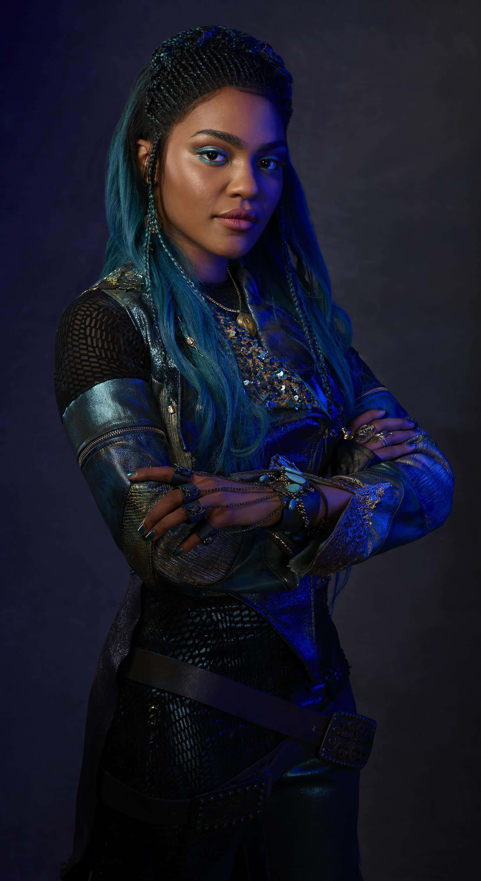 Disney Descendants 桌布 壁紙 — 一位藍髮、身穿華麗盔甲的兇猛女性，在戲劇性的藍色燈光下自信地交叉雙臂站立。