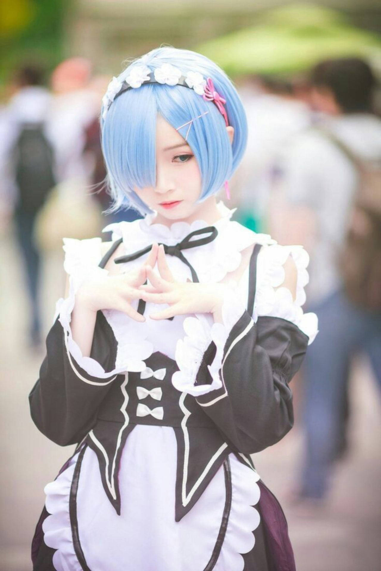 girls 桌布 壁紙 — 一位藍髮女僕裝扮的cosplayer在模糊的戶外人群中用手比出心形。
