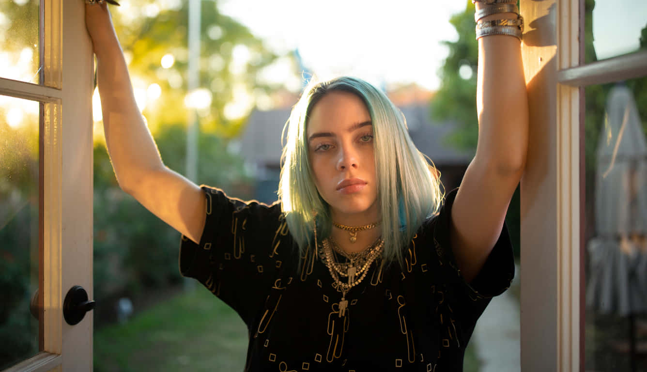 Billie Eilish Laptop 桌布 壁紙 — 一位藍髮年輕女子靠在陽光照射的窗框上，直視鏡頭，表情嚴肅。