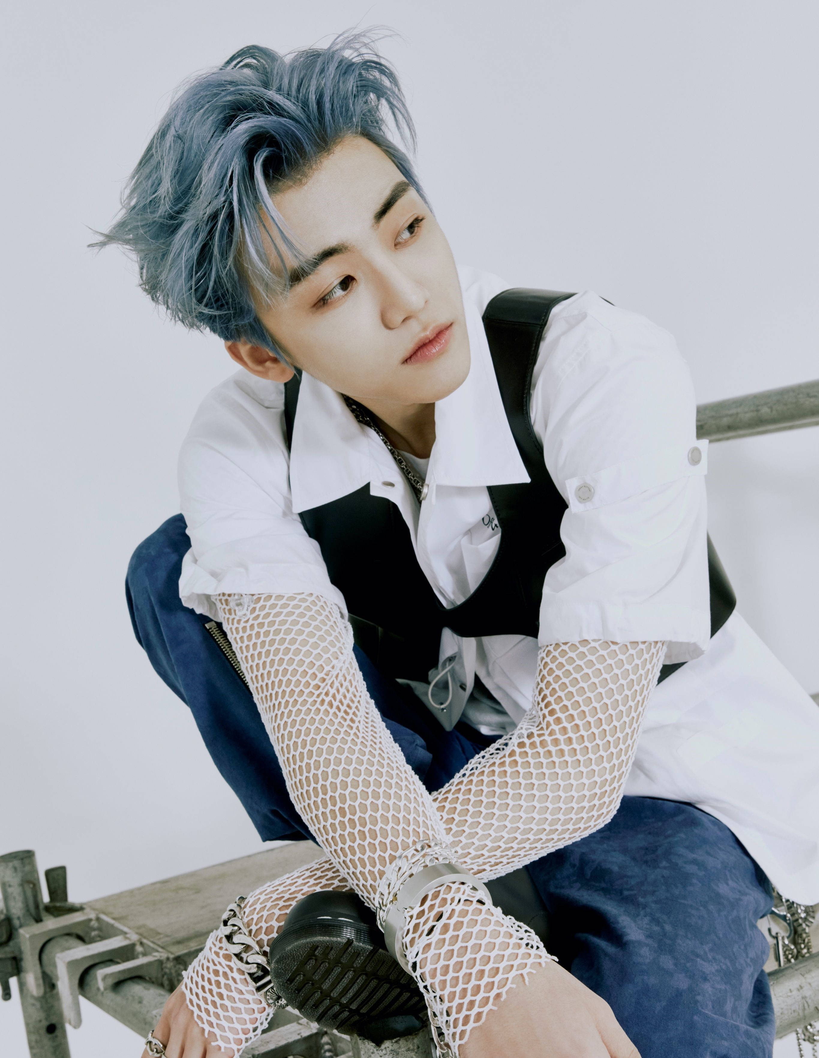 jaemin 桌布 壁紙 — 一位藍髮年輕男子坐在金屬長椅上，身穿白色襯衫、黑色背心和漁網袖套，背景為純白色。
