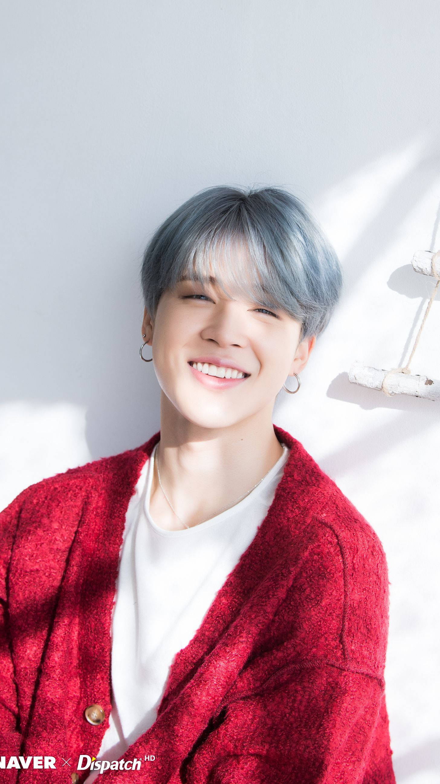 Jimin Bts Cute 桌布 壁紙 — 一位藍髮年輕男子穿著紅色開襟毛衣，在陽光照射的白牆前溫暖微笑。