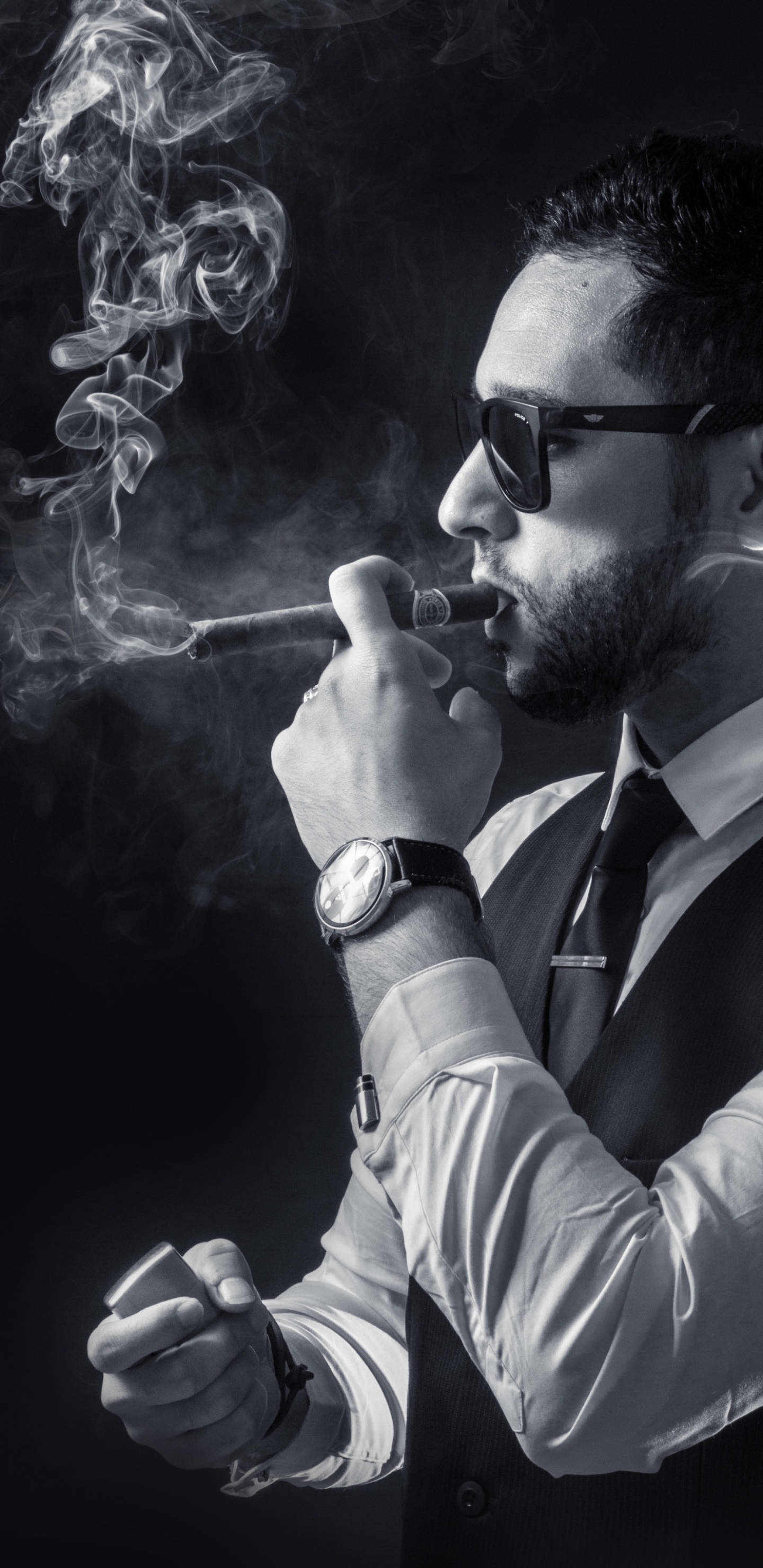 手機 桌布 壁紙 — 一位衣著時尚、戴著太陽眼鏡的男子，在深色背景下手持雪茄和打火機，吐著煙霧。