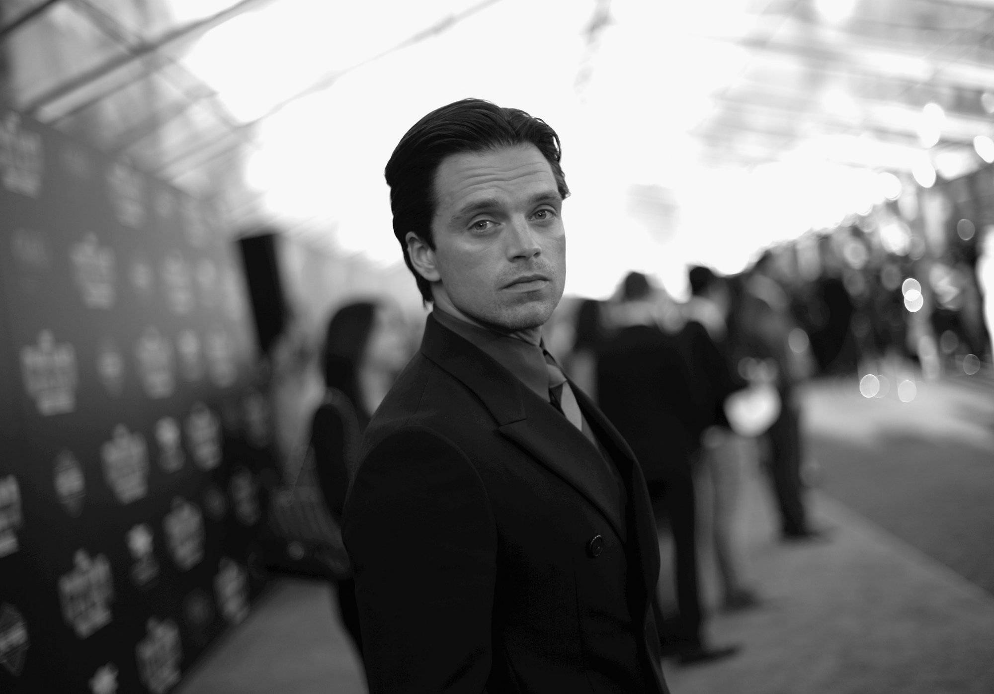 Sebastian 桌布 壁紙 — 一位衣著講究、身穿西裝的男子在明亮的活動燈光下專注地凝視鏡頭，身後是模糊的人群。