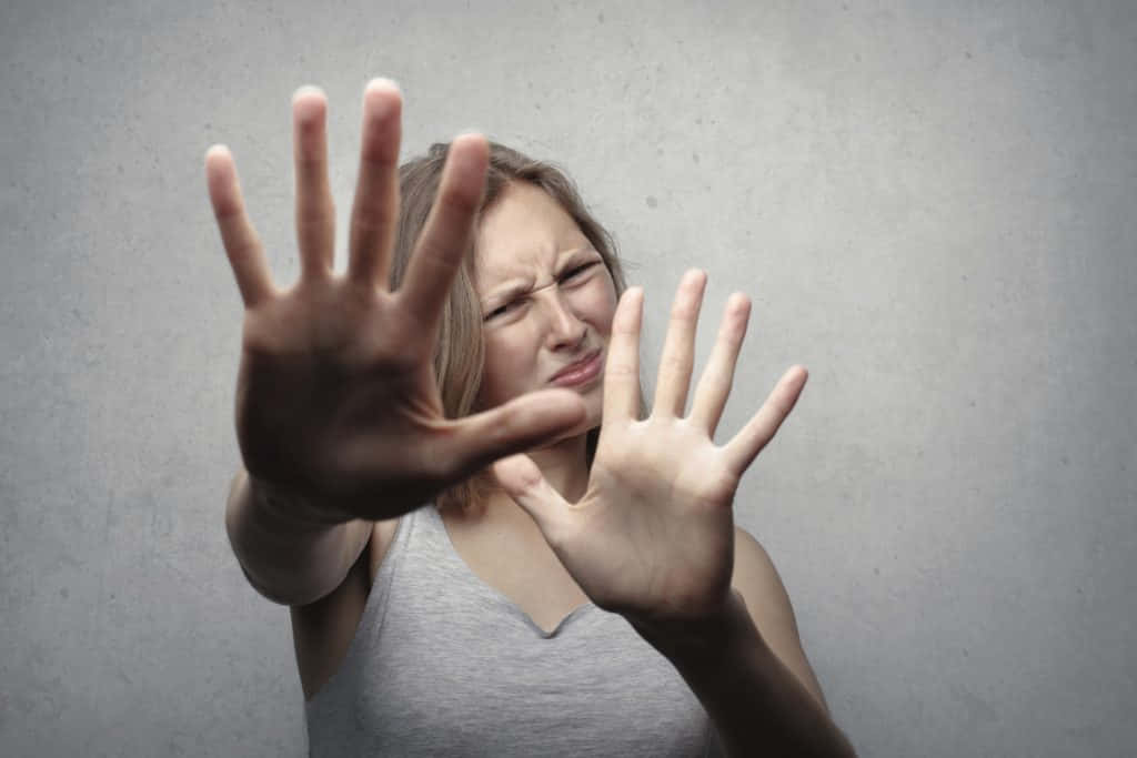 女孩 桌布 壁紙 — 一位表情兇狠的女人雙手向前伸出，做出強烈的停止手勢，背景是純灰色牆壁。