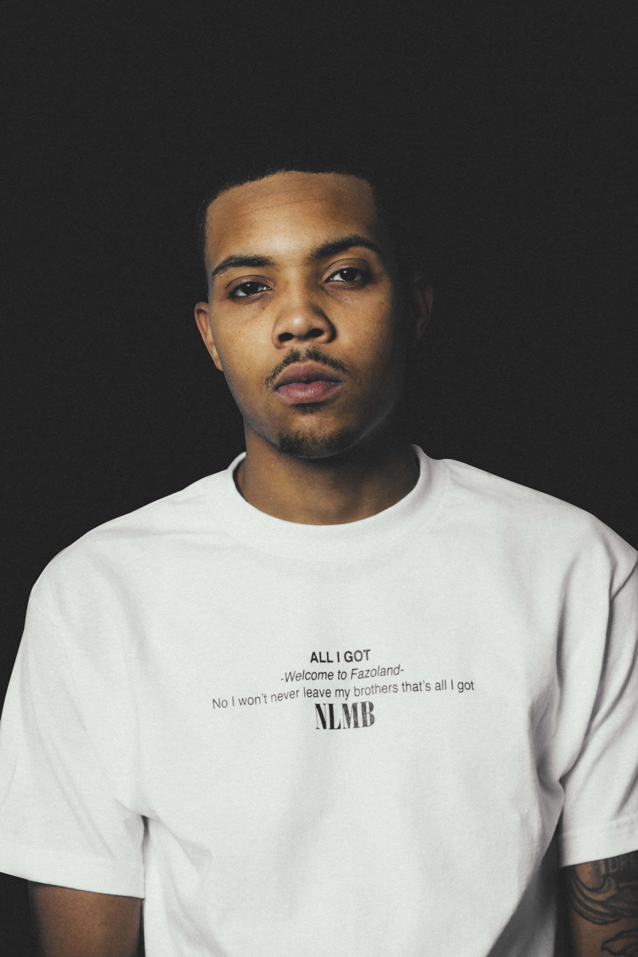 Herbo iPhone 桌布 壁紙 — 一位表情嚴肅的年輕男子穿著白色T恤，上面有粗體黑色文字，背景為深色。