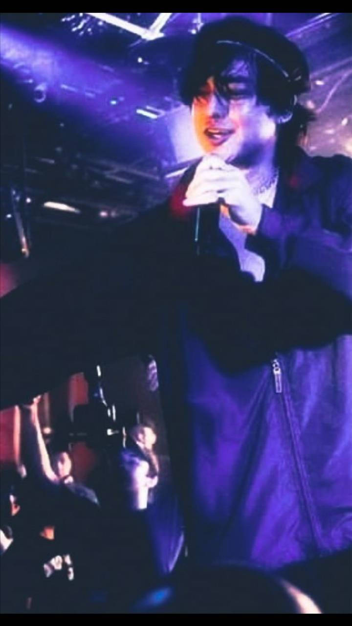 joji 桌布 壁紙 — 一位表演者在紫色燈光的場地中，表情豐富地舉起雙臂對著麥克風唱歌。