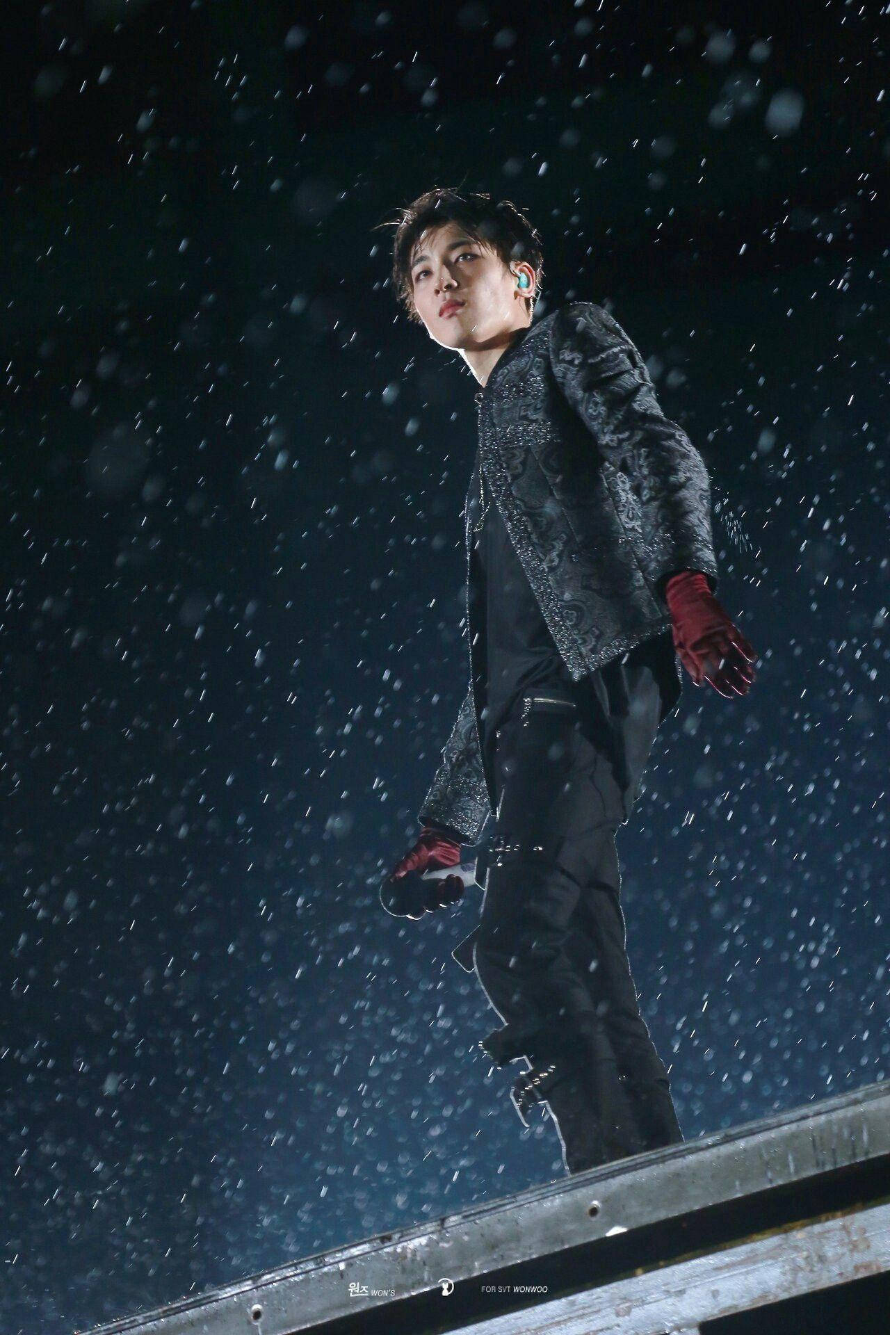 Wonwoo 桌布 壁紙 — 一位表演者夜晚站在舞台上，雪花飄落，身穿深色外套和紅色手套。
