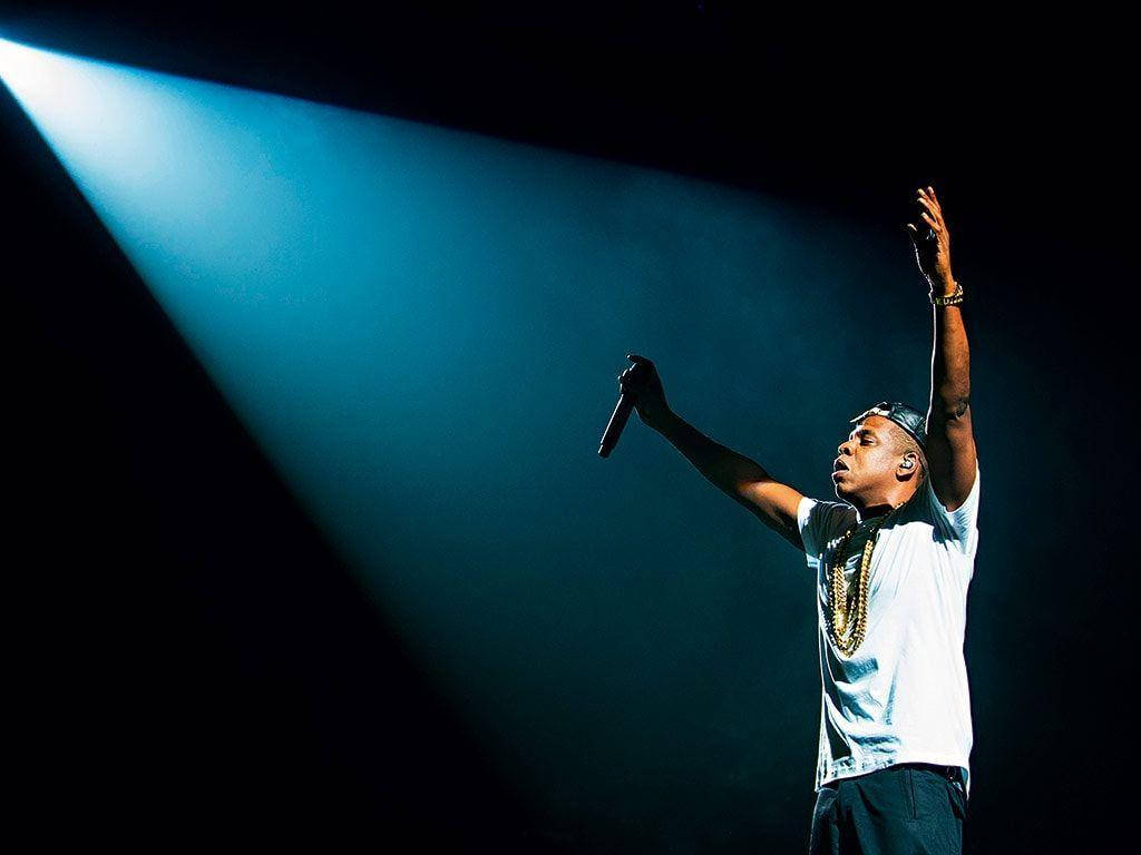 Jay-z 桌布 壁紙 — 一位表演者沐浴在單一藍色聚光燈下，在黑暗的舞台上舉起手臂和麥克風。