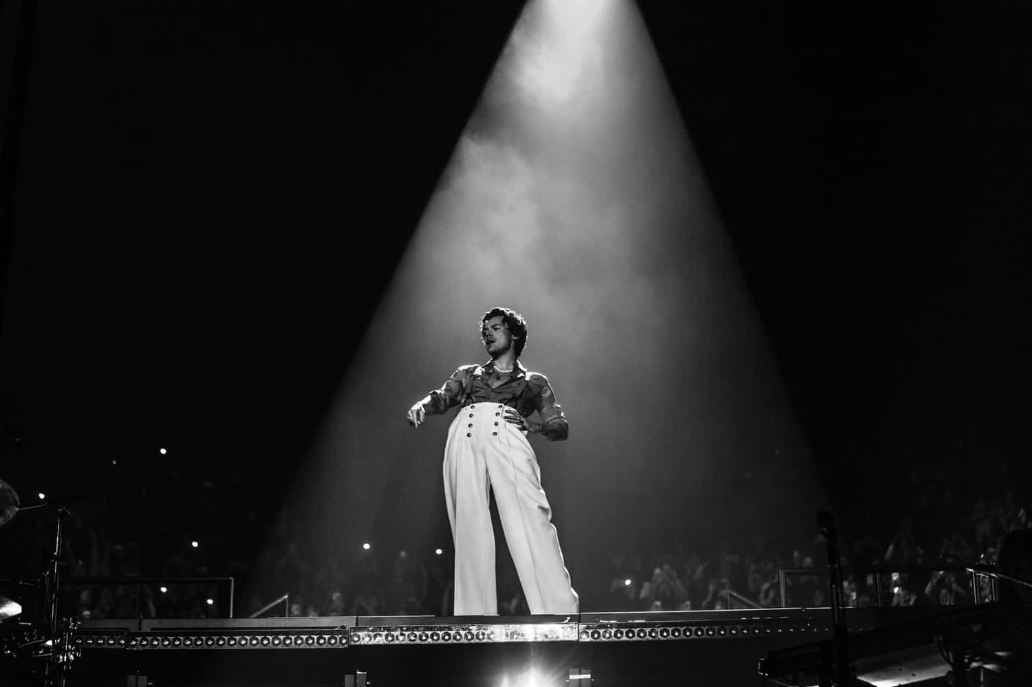Harry Styles Black And White 桌布 壁紙 — 一位表演者獨自站在黑暗演唱會舞台上戲劇性的聚光燈下，背景有群眾。