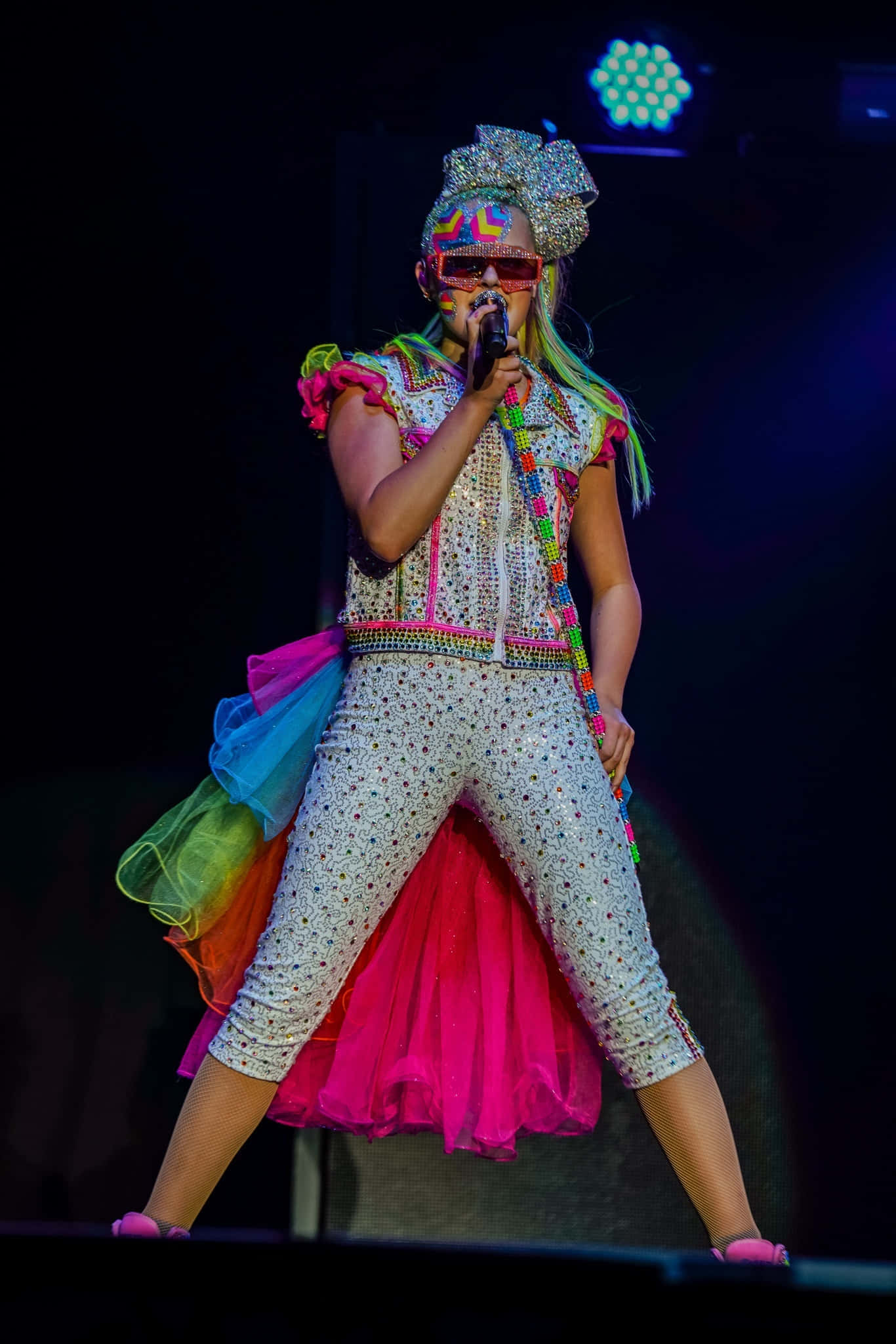 Jojo 桌布 壁紙 — 一位表演者穿著閃閃發光的彩虹服裝，在舞台燈光下對著麥克風唱歌。