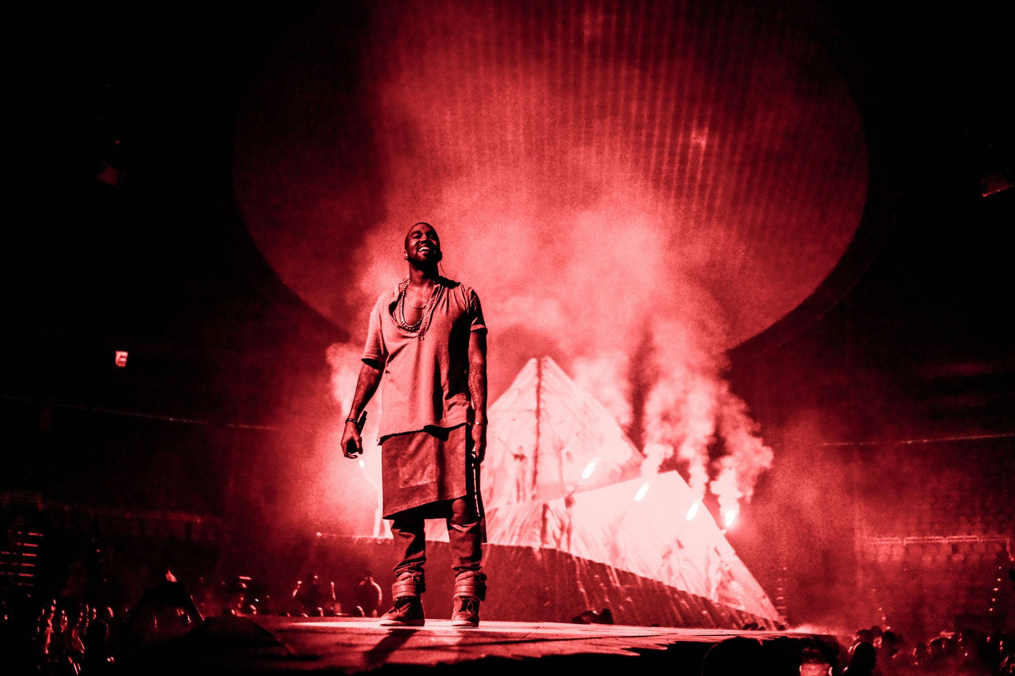 Kanye 桌布 壁紙 — 一位表演者站在被強烈紅光籠罩的舞台上，伴隨著煙霧和發光的金字塔背景。