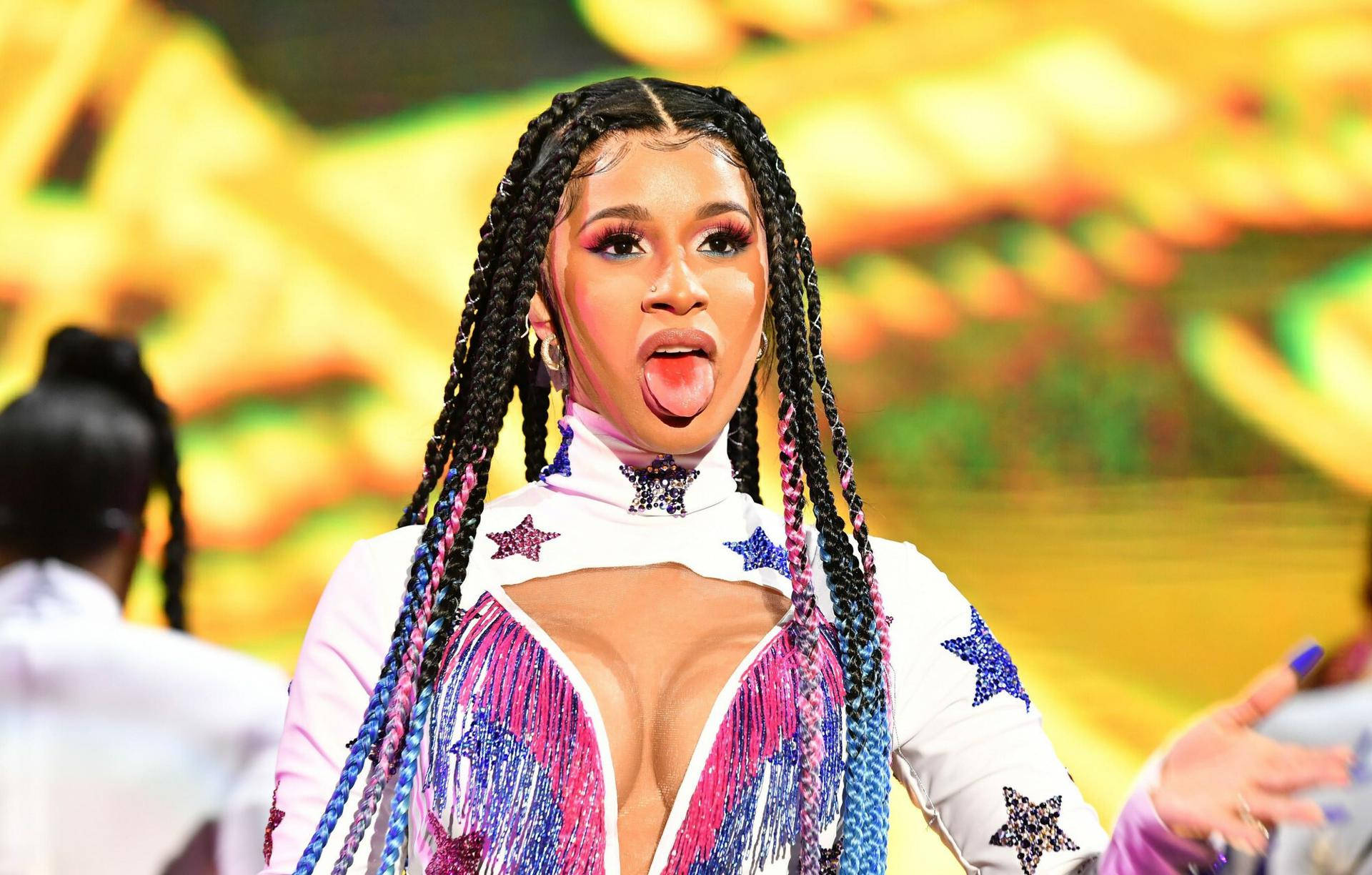 cardi 桌布 壁紙 — 一位表演者紮著辮子，在舞台上穿著閃閃發光的星星裝飾服裝伸出舌頭。