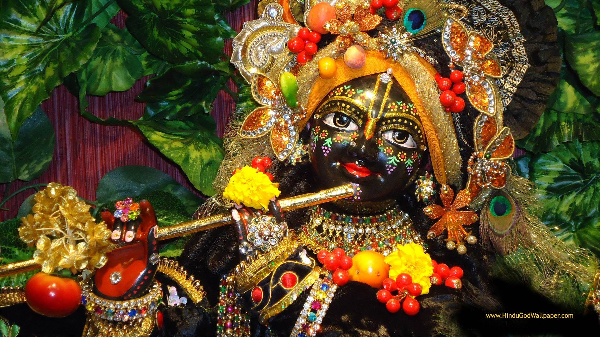 Hindu Temple 桌布 壁紙 — 一位裝飾華麗、佩戴精緻珠寶和花卉裝飾的深色皮膚神祇，在茂密的綠色樹葉背景下吹奏長笛。
