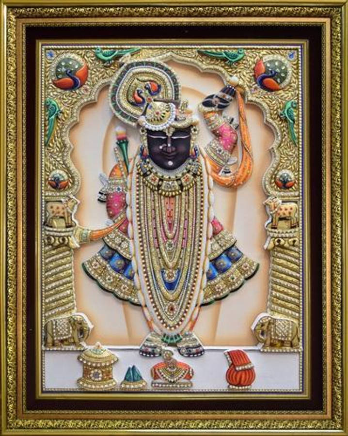 Shrinathji 桌布 壁紙 — 一位裝飾華麗、膚色較深的神祇，佩戴著精緻的珠寶，身處華麗的金色畫框中，在奶油色背景前威嚴地站立。