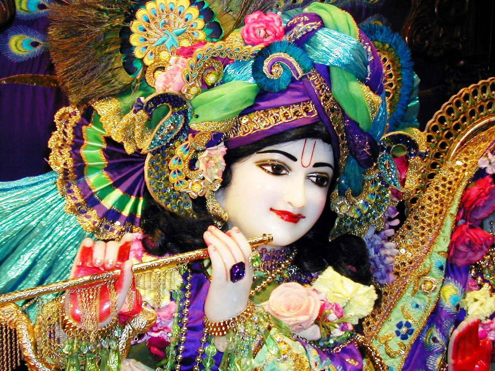 krishna bhagwan 桌布 壁紙 — 一位裝飾華麗的神祇，戴著鑲有寶石的皇冠、孔雀羽毛和一支笛子，神情祥和。