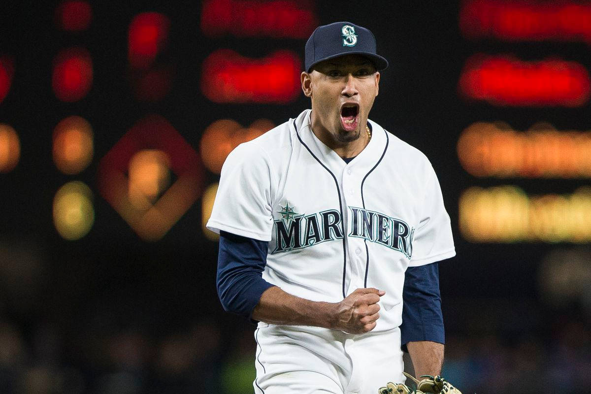 MLB Players 桌布 壁紙 — 一位西雅圖水手隊的棒球選手在夜間比賽中勝利咆哮，身後是模糊的球場燈光。
