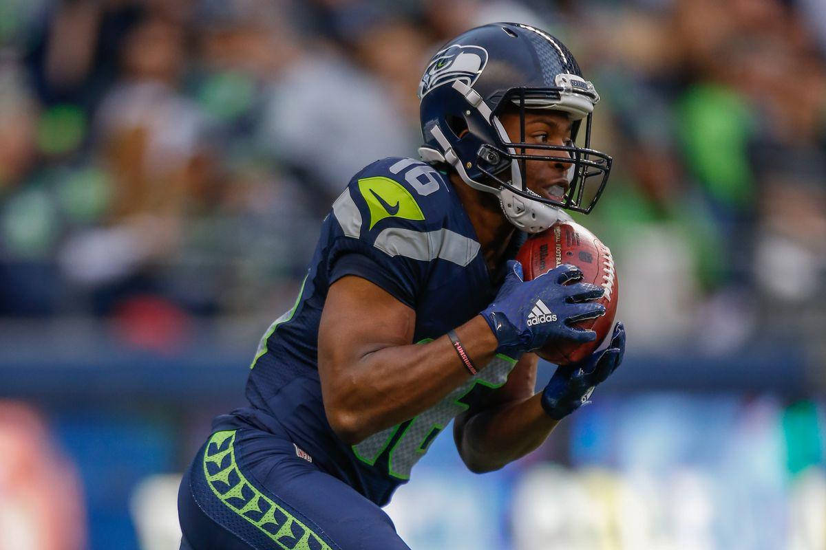 Seattle Seahawks 桌布 壁紙 — 一位西雅圖海鷹隊的美式足球員身穿海軍藍和螢光綠色制服，在日間比賽中持球衝刺。