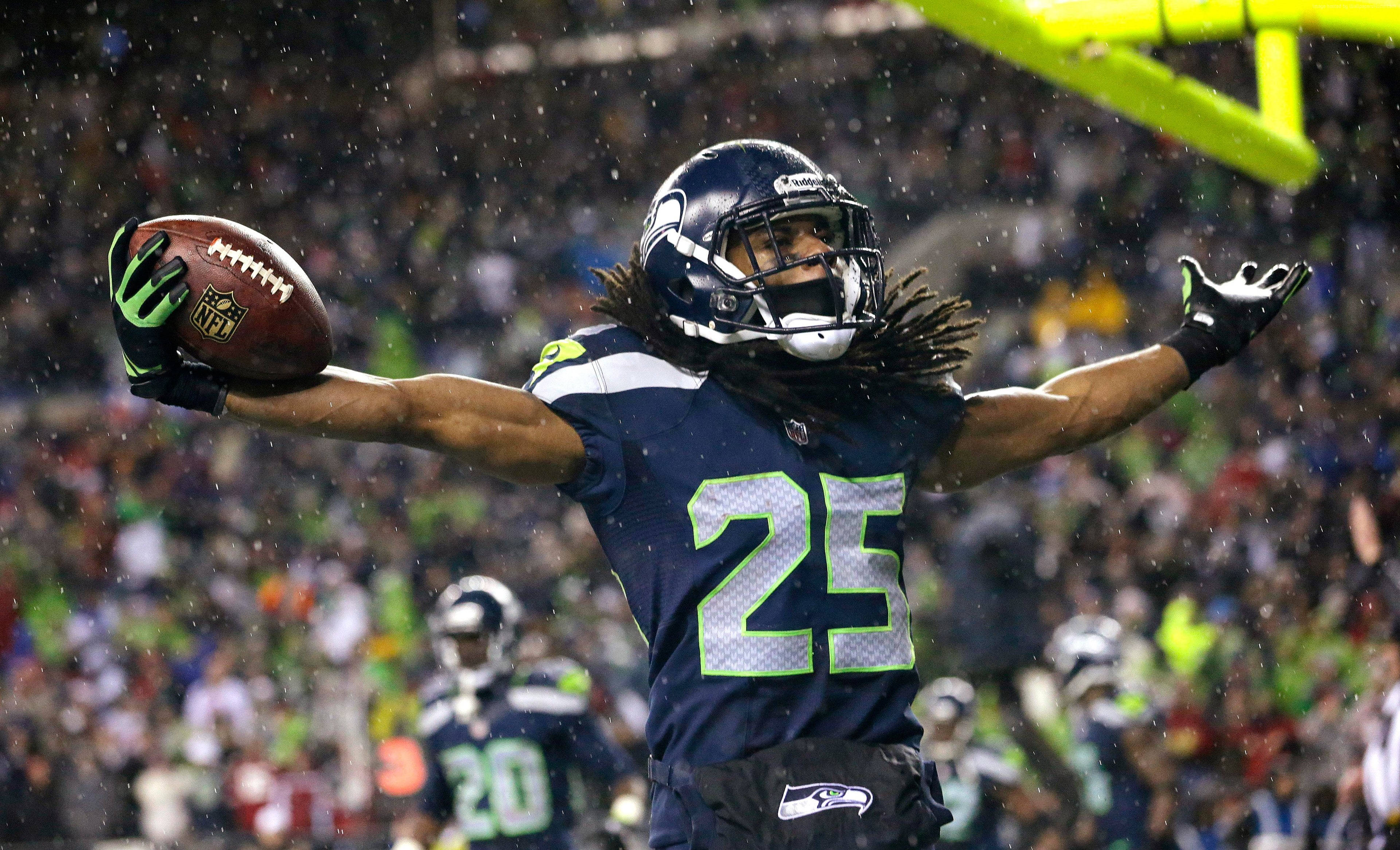Seattle Seahawks 桌布 壁紙 — 一位西雅圖海鷹隊的美式足球球員在雨中張開雙臂，手拿橄欖球，勝利地慶祝。
