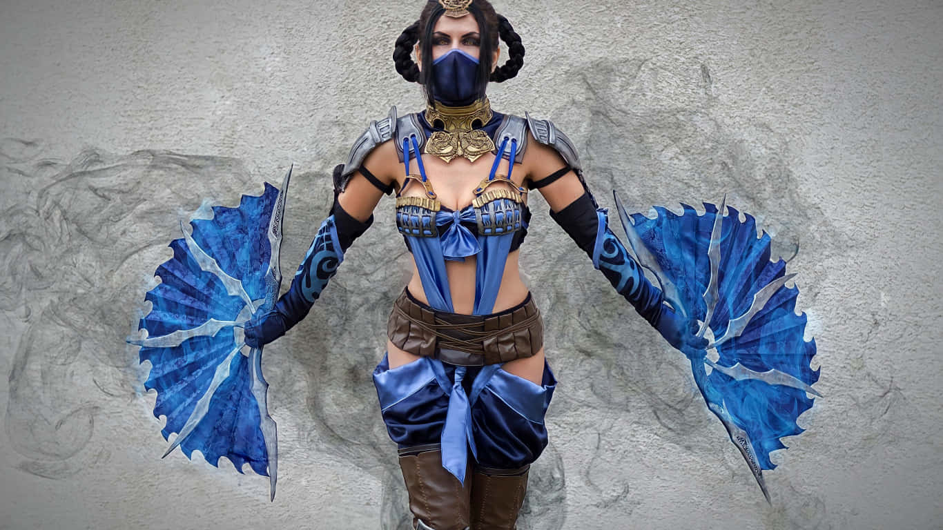 Mortal Kombat Cosplays 桌布 壁紙 — 一位角色扮演者身穿精緻的藍金色奇幻戰士服裝，手持華麗扇子，站在有紋理的石牆前。