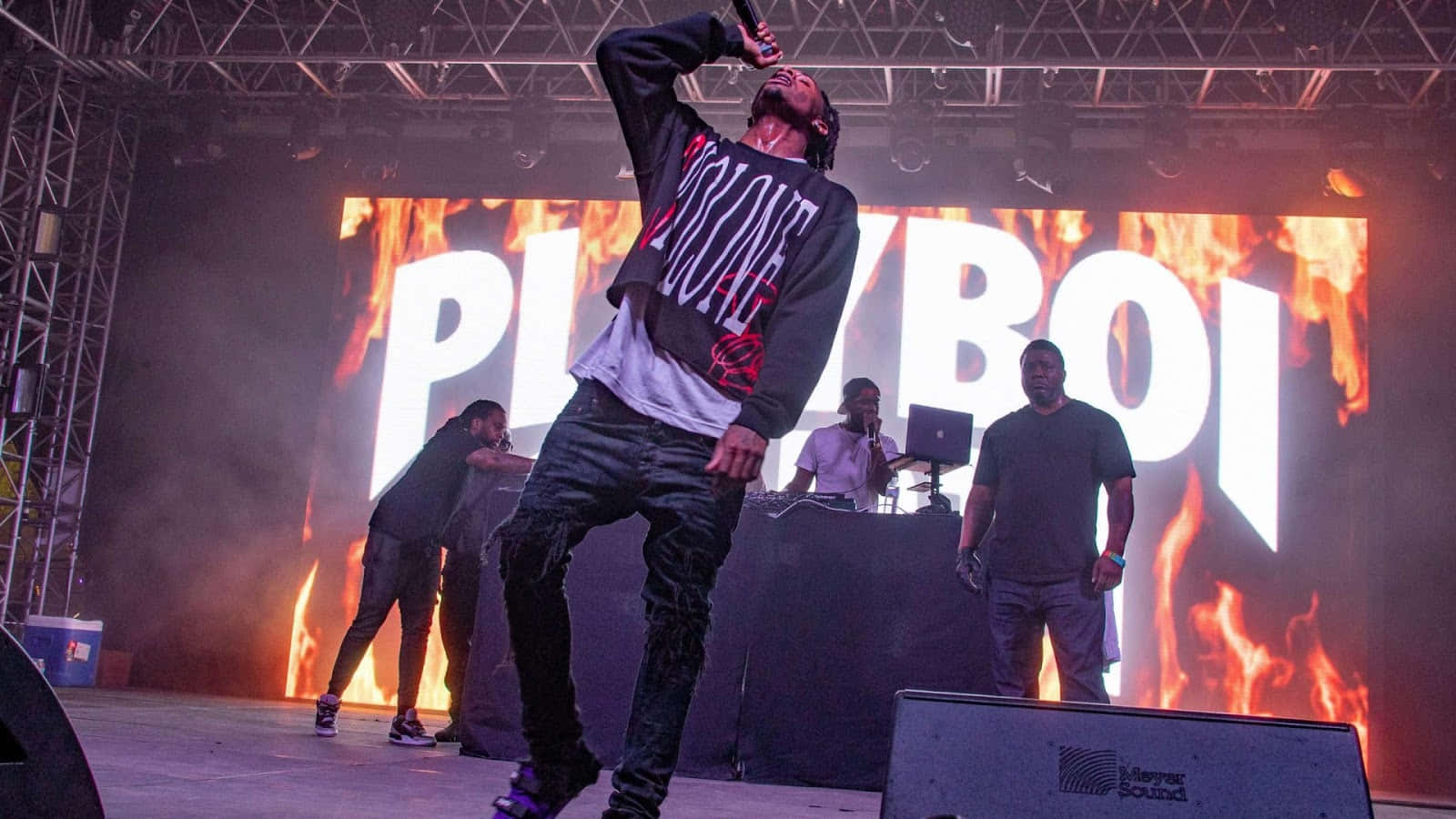 Playboi Carti 桌布 壁紙 — 一位說唱歌手在舞台上充滿活力地表演，背景是火熱的「PLAYBOI」字樣和煙霧效果。