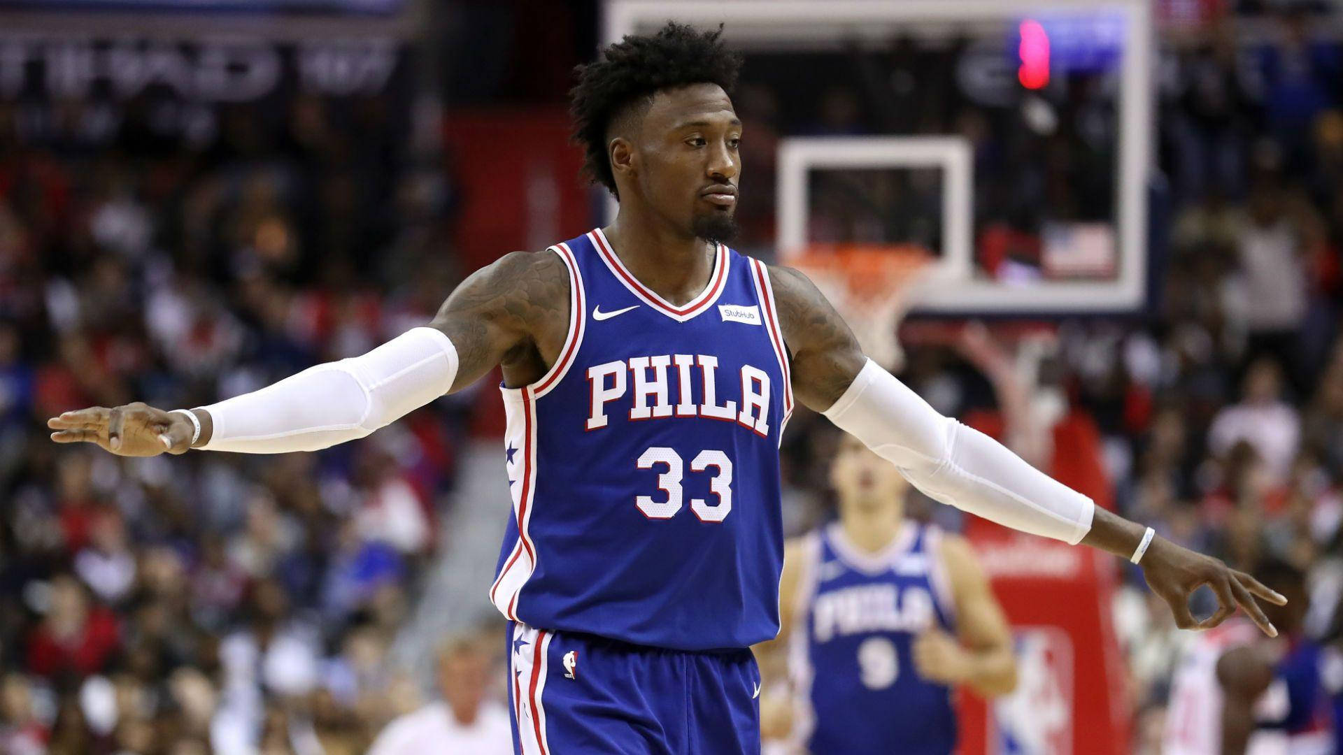 robert covington 桌布 壁紙 — 一位費城76人籃球運動員身穿藍色球衣33號，在比賽期間於擁擠的球場上張開雙臂站立。