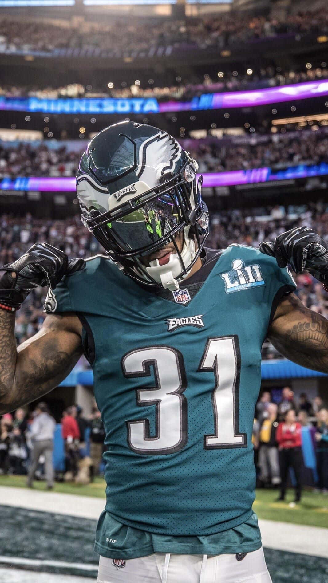 Eagles Football 桌布 壁紙 — 一位費城老鷹隊的美式足球員，身穿青綠色31號球衣，在燈光璀璨、座無虛席的體育館中勝利歡呼。