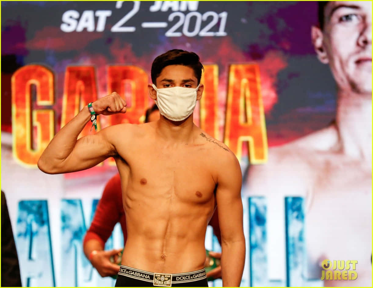 Ryan Garcia 桌布 壁紙 — 一位赤膊的肌肉男在拳擊過磅活動中，戴著白色口罩展示二頭肌。
