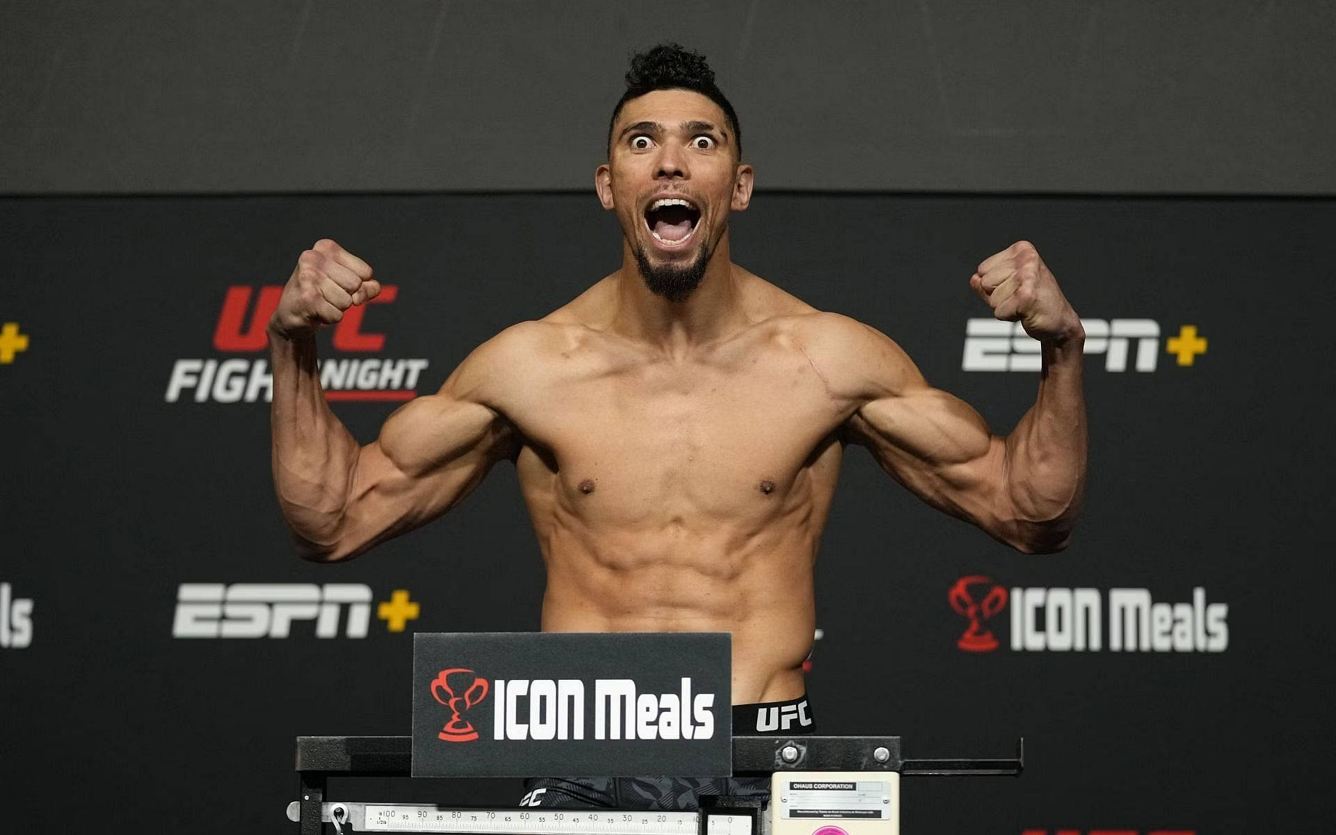MMA 桌布 壁紙 — 一位赤膊的肌肉發達戰士在明亮的燈光下於UFC稱重活動中舉起拳頭慶祝。