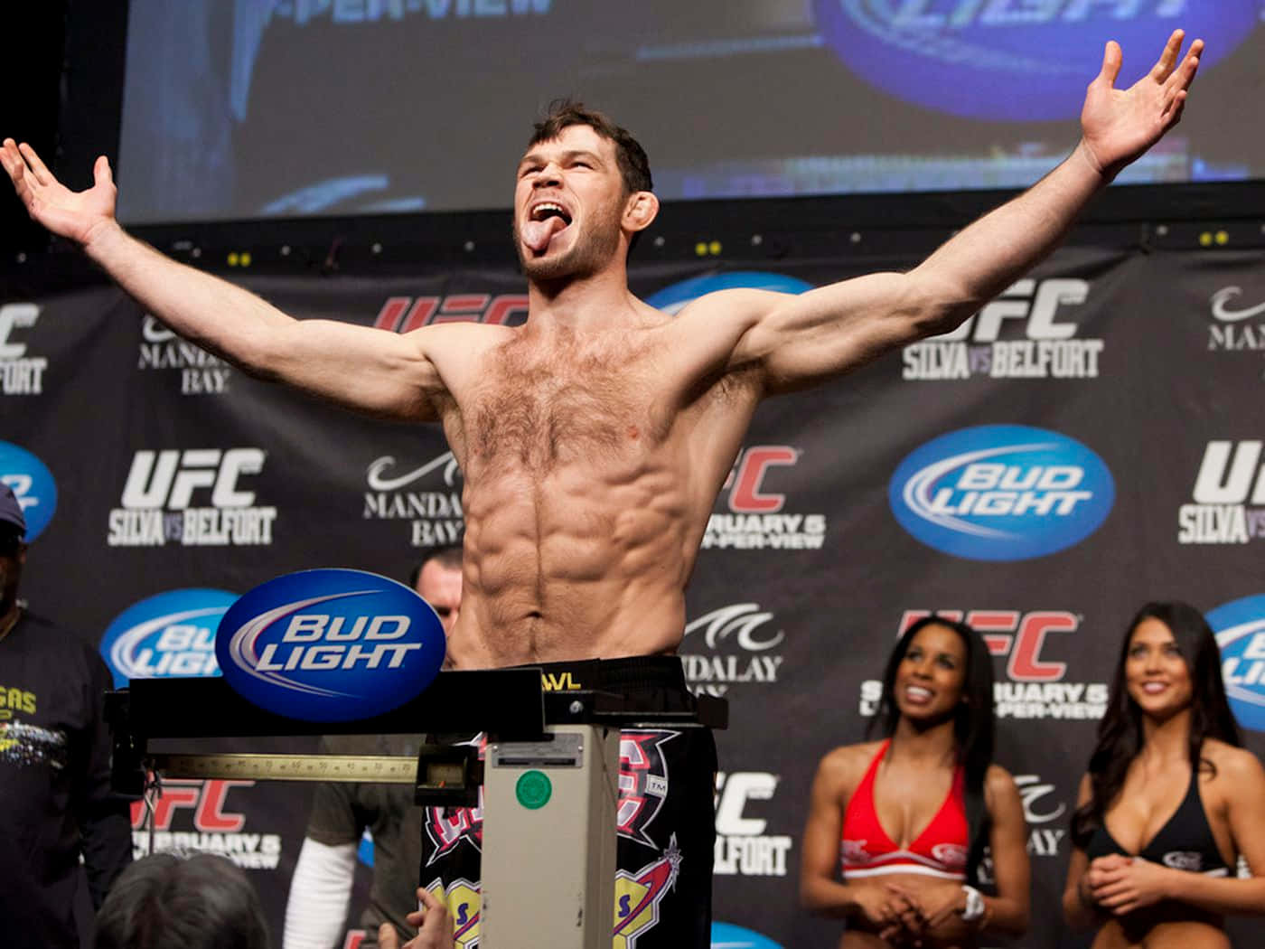 UFC 桌布 壁紙 — 一位赤膊肌肉發達的拳手在UFC過磅活動中高舉雙臂、伸出舌頭，勝利地慶祝。