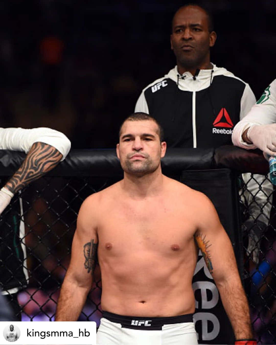 Champion 桌布 壁紙 — 一位赤裸上身、有刺青的MMA拳手站在UFC八角籠內，在明亮的場館燈光下。