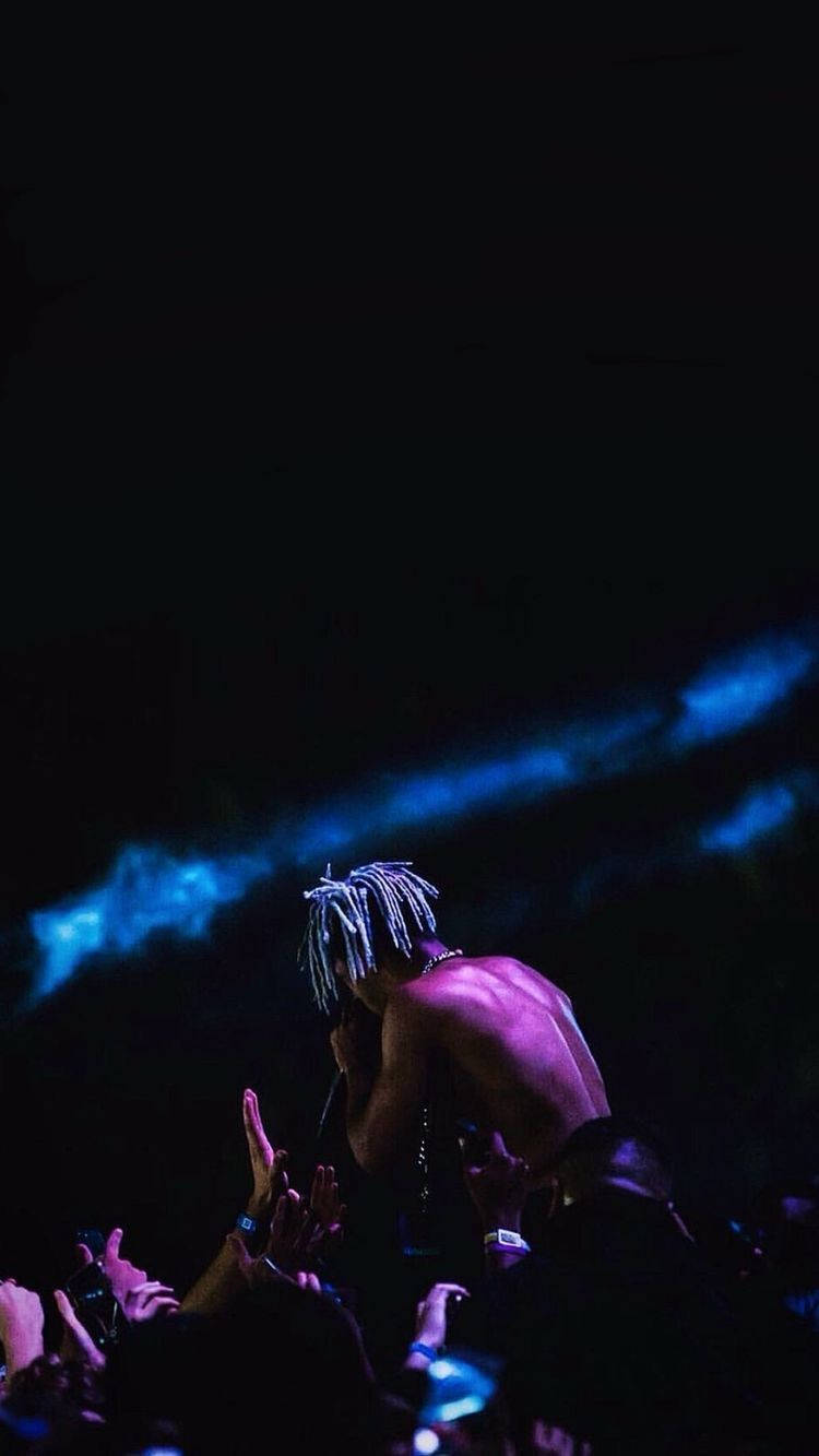 xxxtentacion 美學 桌布 壁紙 — 一位赤裸上身、編髮的表演者在藍色舞台燈光下對著麥克風唱歌，粉絲們在黑暗中伸手向他。