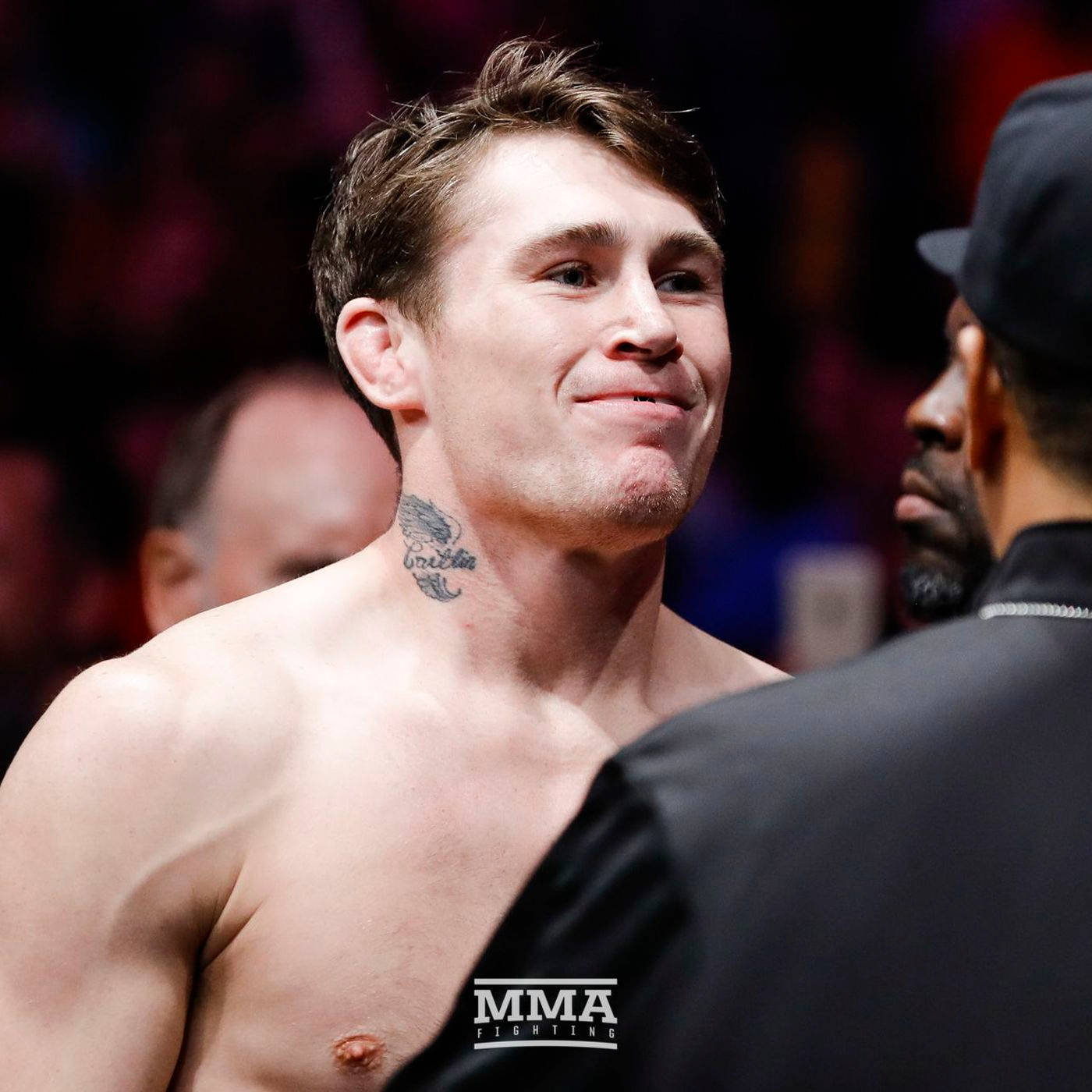 UFC 桌布 壁紙 — 一位赤裸上身的MMA拳手，頸上有刺青，在場館燈光下於賽前面對面對峙中自信地微笑。