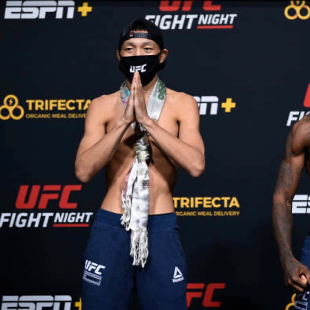 UFC 桌布 壁紙 — 一位赤裸上身的UFC拳手，穿著藍色短褲和黑色口罩，在稱重活動中以雙手合十的姿勢表示尊重。