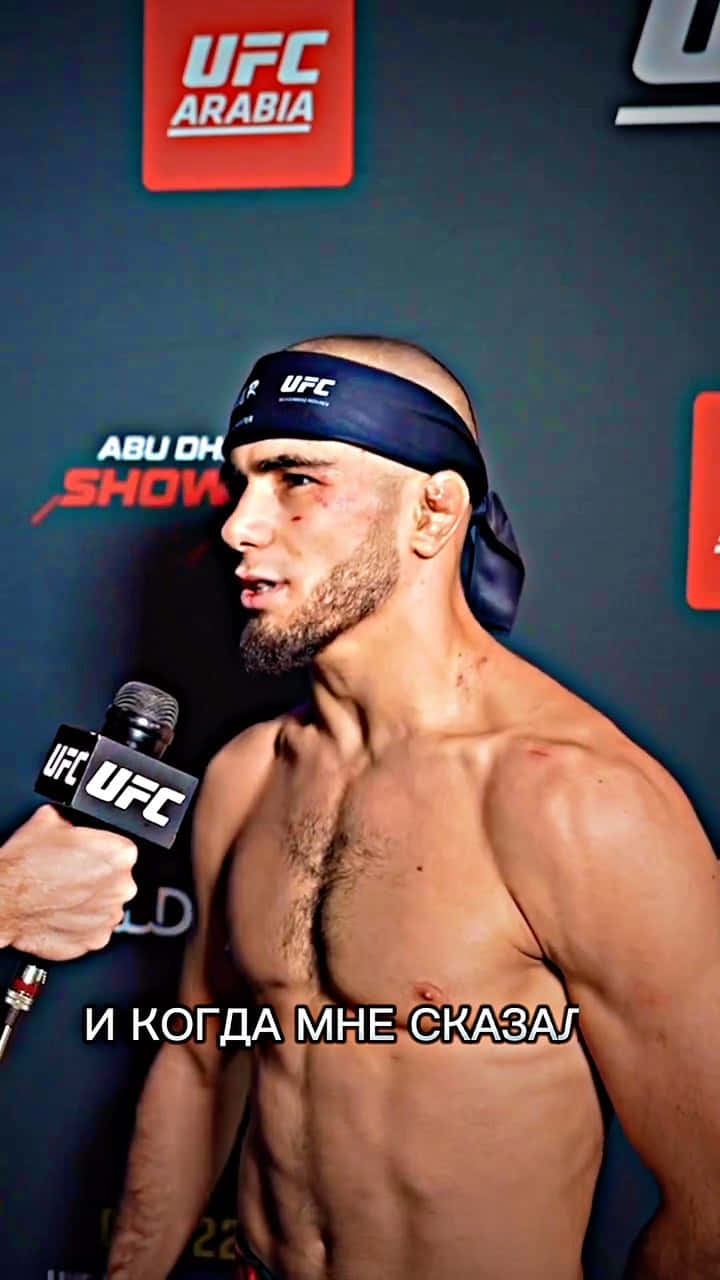 MMA 桌布 壁紙 — 一位赤裸上身的UFC拳手，臉上帶血並戴著頭帶，在記者會上對著麥克風說話。