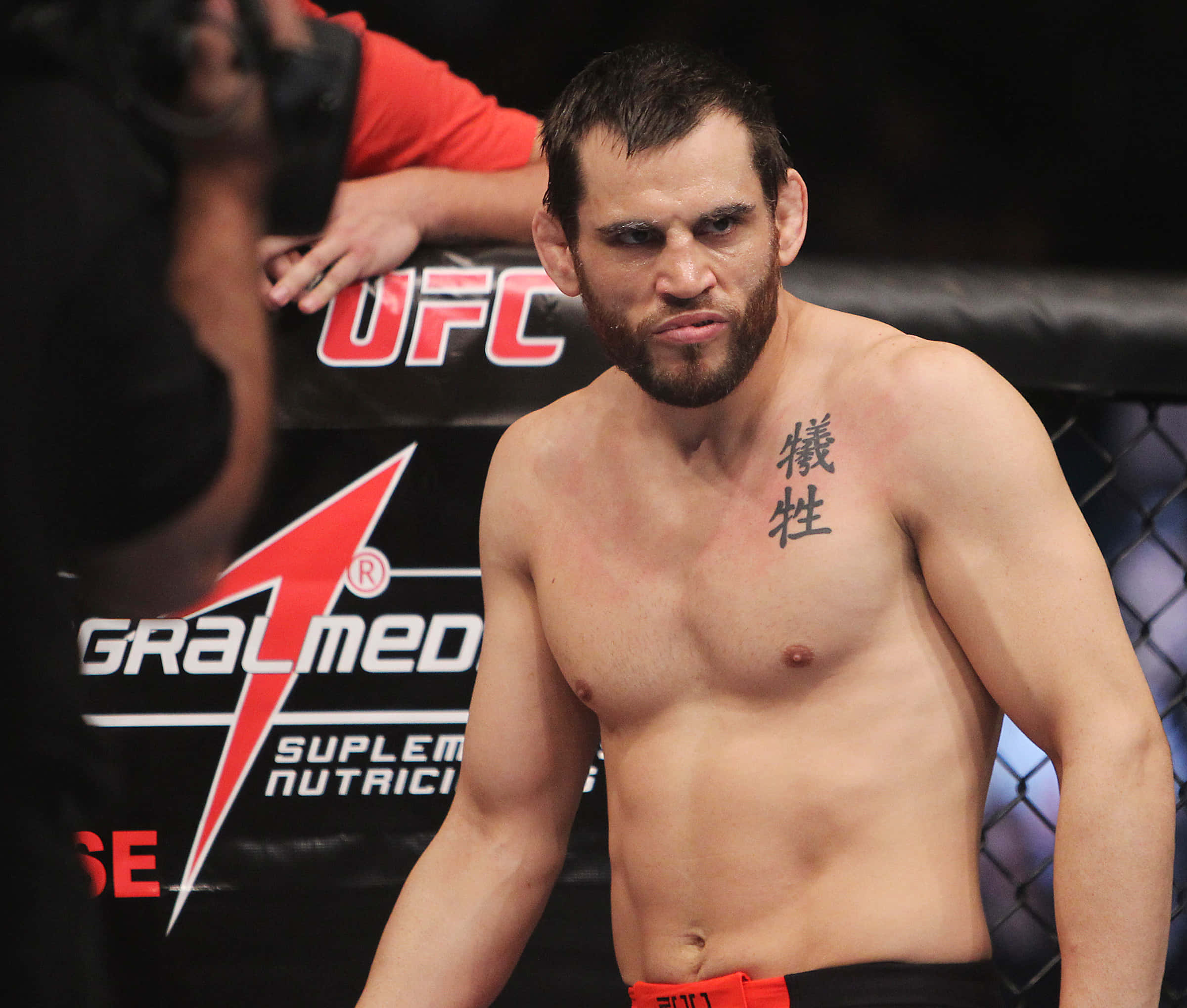 UFC 桌布 壁紙 — 一位赤裸上身的UFC拳手，表情嚴肅，胸前紋有中文字，站在八角籠內。