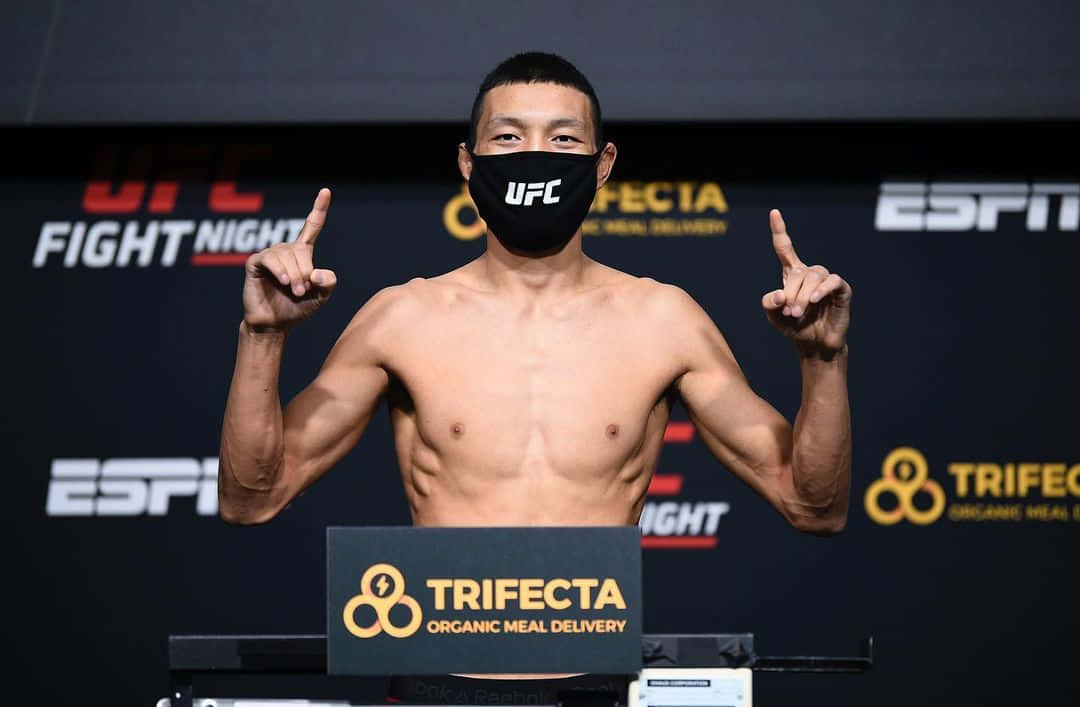 MMA 桌布 壁紙 — 一位赤裸上身的UFC拳手戴著黑色口罩，在稱重活動中舉起雙食指做手勢。