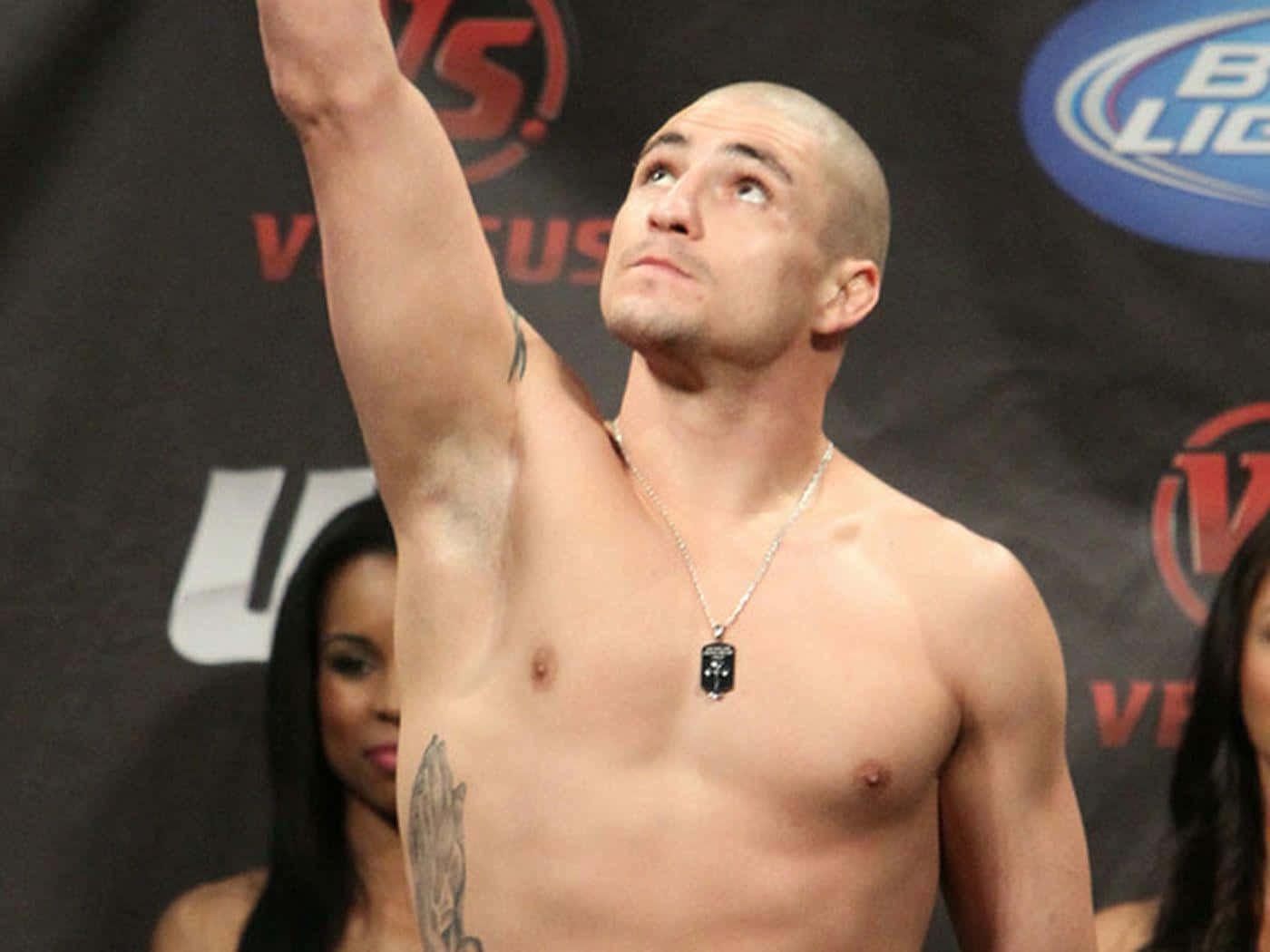 MMA 桌布 壁紙 — 一位赤裸上身的光頭拳擊手在UFC品牌背景的稱重活動中勝利地舉起手臂。