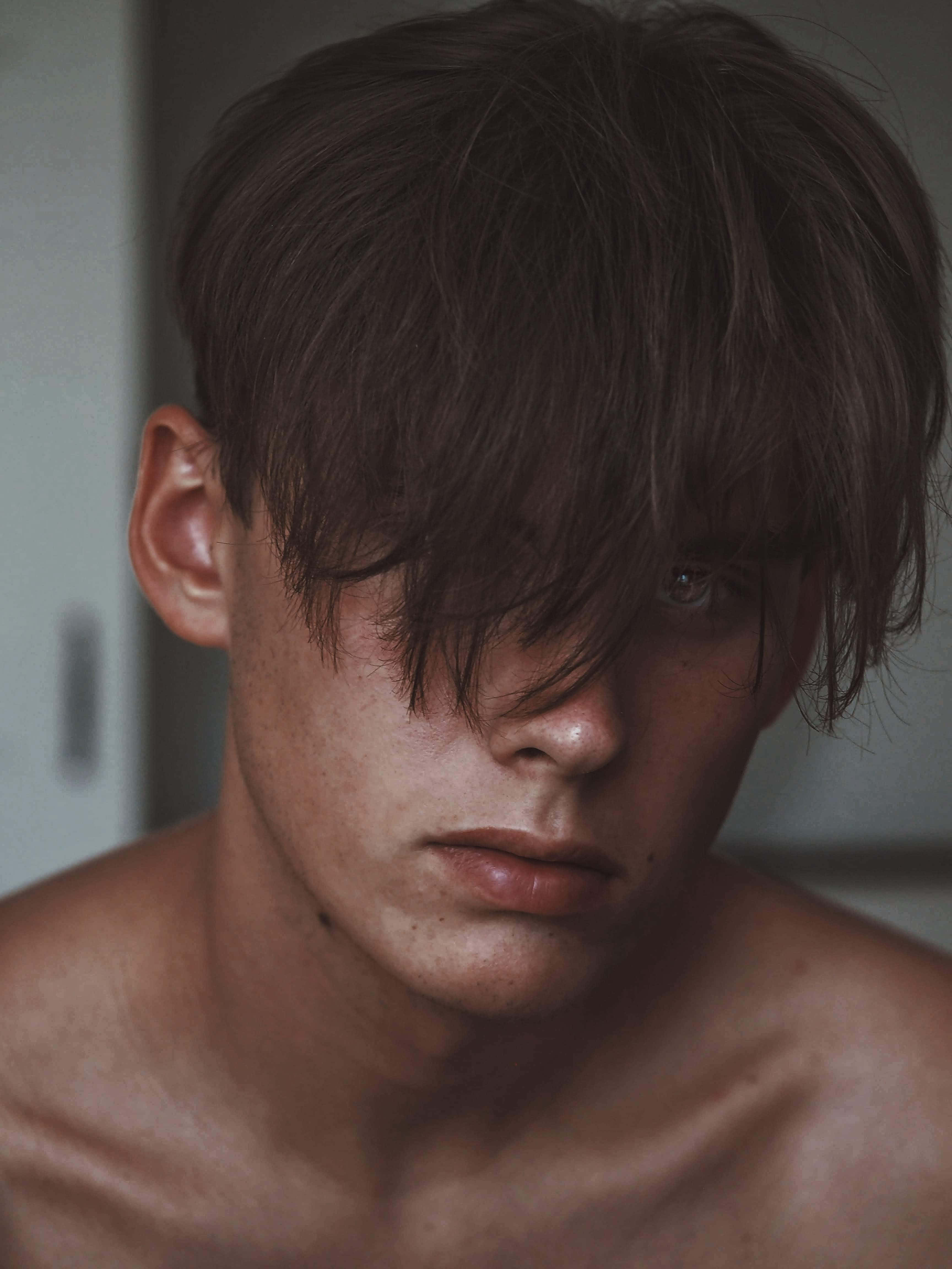 Hot Guy 桌布 壁紙 — 一位赤裸上身的年輕男子，深色凌亂的頭髮部分遮蓋了他的臉龐，在柔和光線的室內環境中專注地凝視。