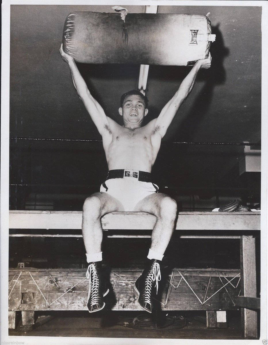 Boxing 桌布 壁紙 — 一位赤裸上身的拳擊手坐在木凳上，在昏暗的健身房中將沉重的沙袋舉過頭頂。
